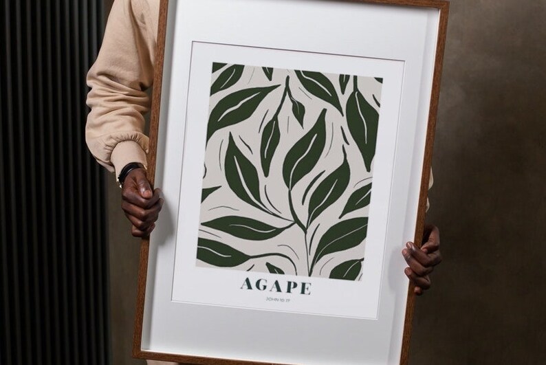 May include: A framed print with a white background and a green leaf pattern. The print has the word "AGAPE" in dark green text and the words "John 13:34" in smaller dark green text.