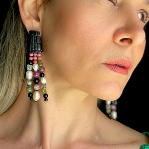 Peut inclure: Une femme portant une robe sans manches verte avec des détails en dentelle, regardant vers la droite. Elle porte de longues boucles d'oreilles pendantes avec des perles noires, blanches et vertes.