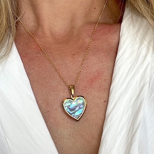 Puede incluir: Un collar de cadena dorada con un colgante en forma de corazón. El colgante está hecho de nácar iridiscente.