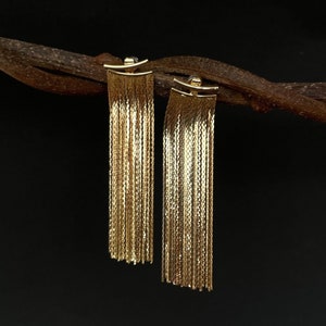 May include: A pair of gold dangle earrings with a chain link design. The earrings are hanging from a brown branch.