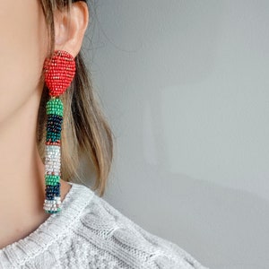 May include: A pair of long, colorful beaded earrings with a red heart-shaped bead at the top. The earrings are made with green, white, black, and red beads.