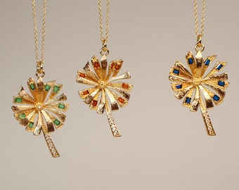May include: Three gold necklaces with palm tree pendants. Each pendant has a different colored gemstone: green, orange, and blue.