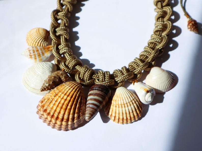 May include: A gold rope necklace with various seashells attached. The shells are in shades of white, brown, and tan.