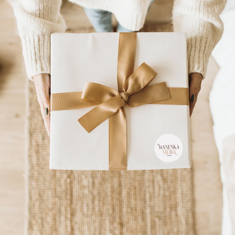 May include: A white gift box with a gold ribbon and bow. A white sticker with the text "Waneska Vieira" is on the box.