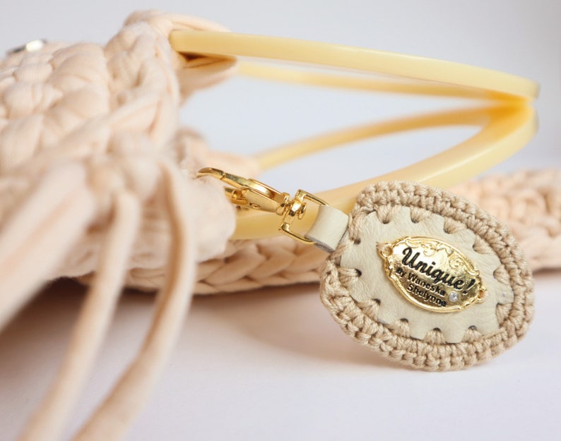 May include: A beige crocheted bag with a cream-colored leather tag that says "Unique! by Wioletta Szylypko" with a small rhinestone.