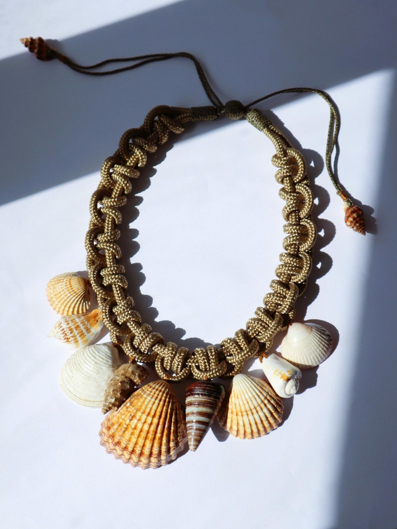 May include: A brown and gold rope necklace with a variety of seashells attached. The shells are in shades of brown, white, and tan.