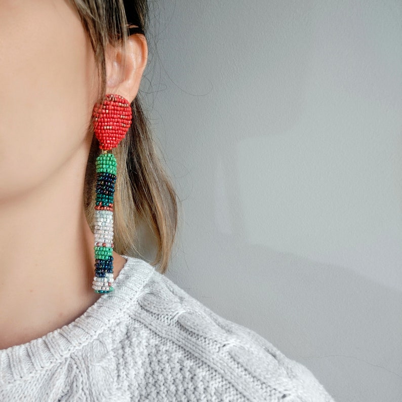 May include: A pair of long, colorful beaded earrings with a red heart-shaped bead at the top. The earrings are made with green, white, black, and red beads.