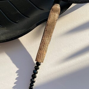 May include: A gold pendant necklace with a textured, rectangular charm and a long strand of black beads.