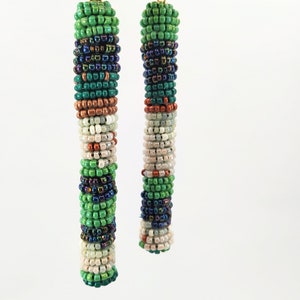 May include: A pair of long, beaded earrings with a multi-colored pattern. The earrings are made with green, blue, white, and copper beads.