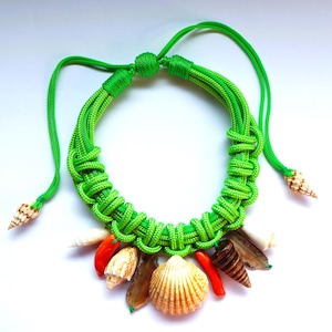 May include: A green rope necklace with a variety of seashells attached. The shells are in shades of brown, white, and orange.