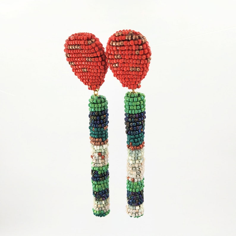 May include: A pair of long, beaded earrings with red, green, white, and blue beads. The top of each earring is a red, beaded teardrop shape.