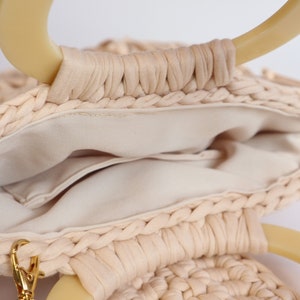 May include: A cream-colored woven bag with two large, cream-colored handles. The bag has a cream-colored fabric lining and a small pocket inside.