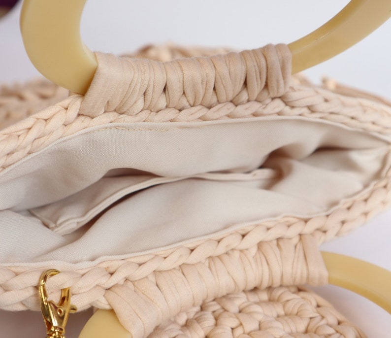 May include: A cream-colored woven bag with two large, cream-colored handles. The bag has a cream-colored fabric lining and a small pocket inside.