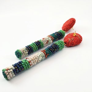 May include: A pair of long, beaded earrings with a red heart-shaped bead at the bottom of each earring. The beads are in shades of green, white, blue, and orange.