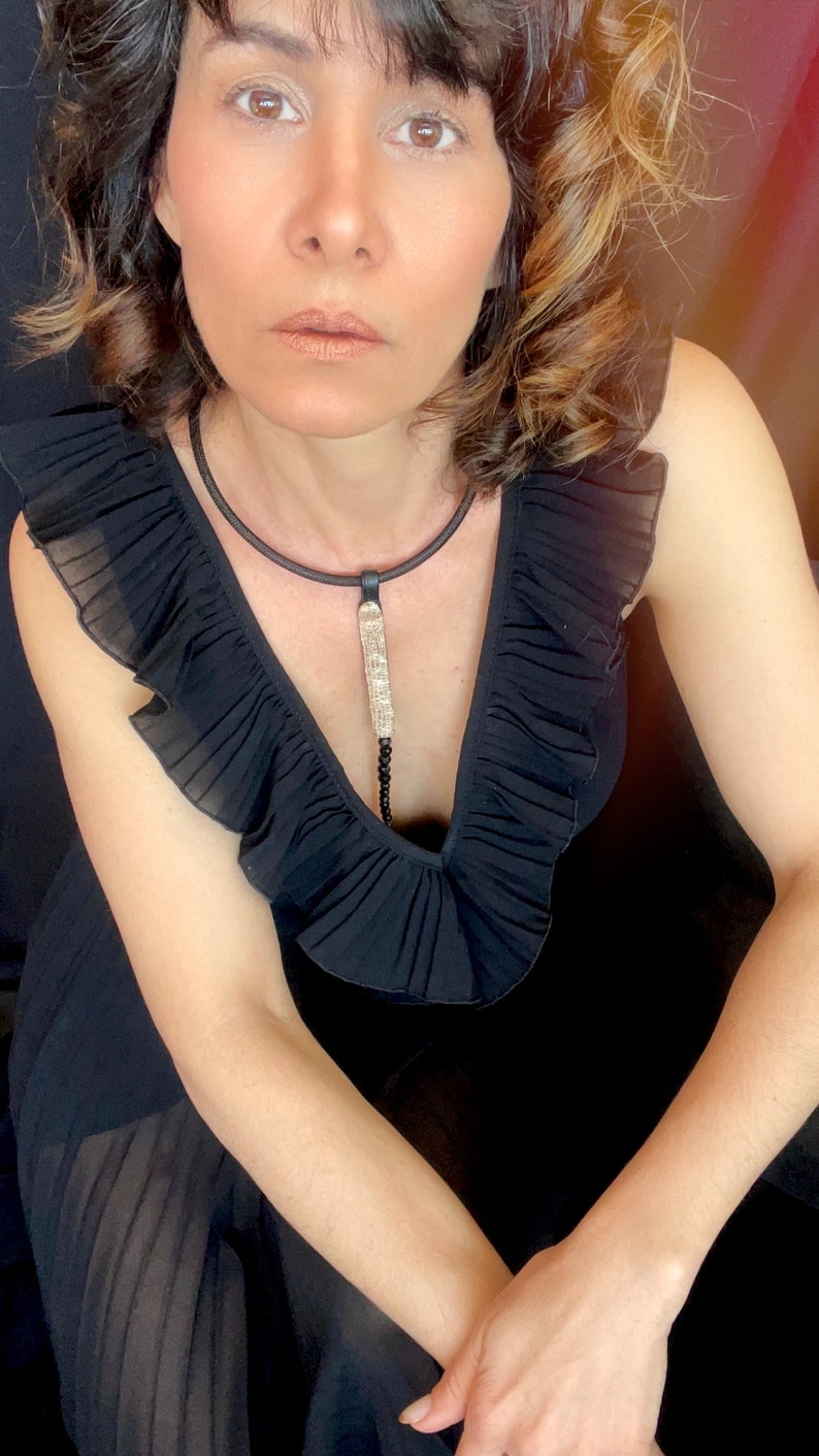 May include: A woman wearing a black ruffled dress with a long, silver and black pendant necklace.