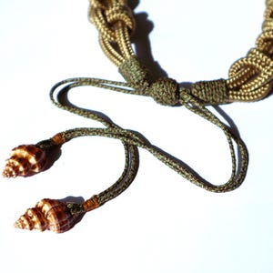 May include: A brown and gold rope necklace with two brown seashells attached to the ends.