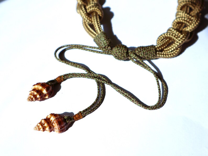May include: A brown and gold rope necklace with two brown seashells attached to the ends.