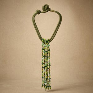 Peut inclure: Un collier composé d'un cordon épais vert olive avec une fermeture à nœud et un groupe central de multiples brins pendants. Ces brins sont constitués de petites perles rondes dans diverses nuances de vert, du vert citron clair au vert forêt.