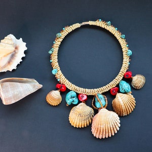 May include: A gold necklace with turquoise and red beads and seashells. The necklace is on a black background.