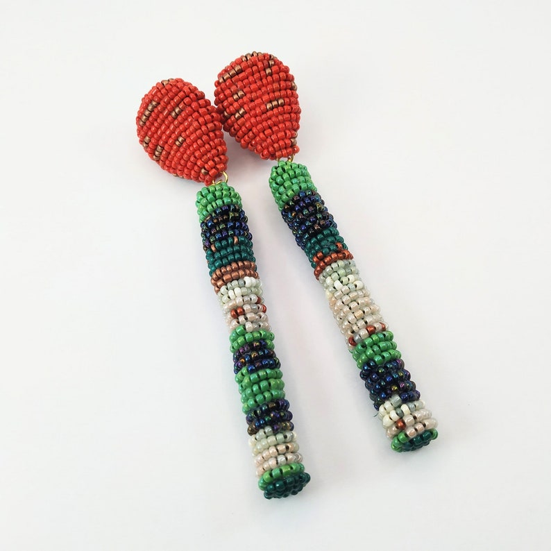 May include: A pair of long, beaded earrings with a red teardrop-shaped bead at the top and a multi-colored beaded design in shades of green, white, and black.