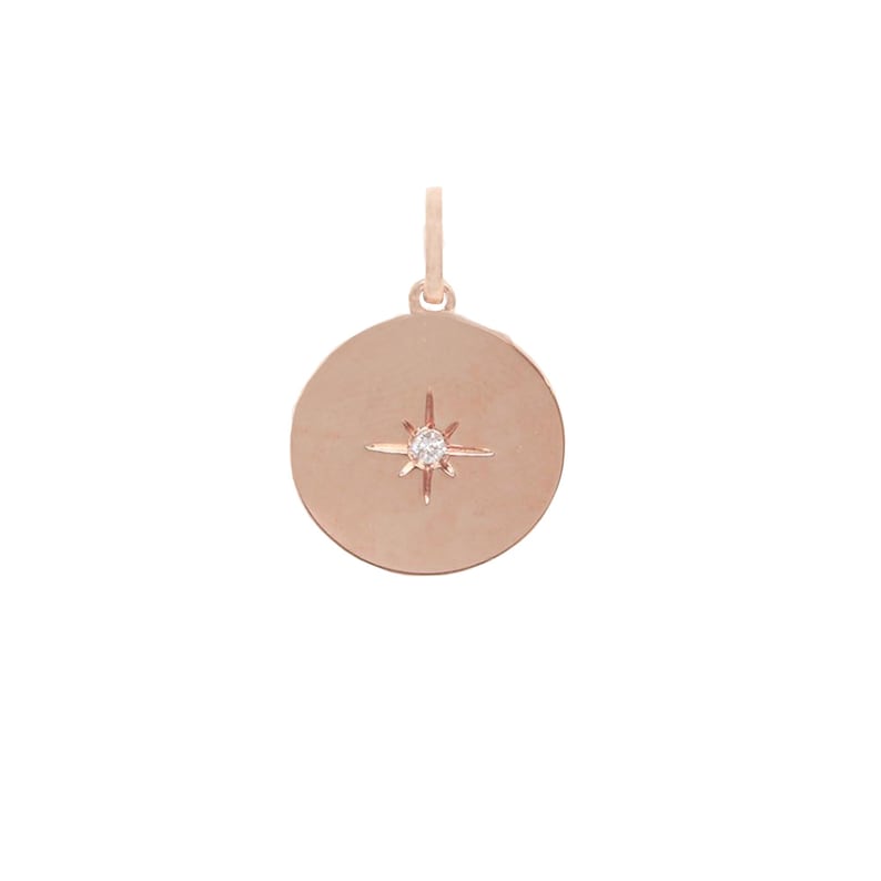 Puede incluir: Colgante de oro rosa con dise&ntilde;o circular. El colgante presenta un dise&ntilde;o de estrella con una peque&ntilde;a gema redonda y transparente en el centro. El colgante tiene un peque&ntilde;o lazo en la parte superior para una cadena.