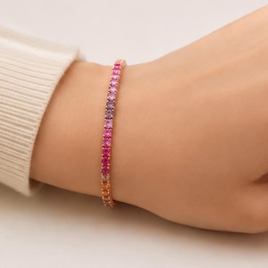 May include: A delicate bracelet featuring a gradient of colorful gemstones, transitioning from orange to pink and purple. The bracelet is set in a gold-toned metal, creating a vibrant and elegant accessory. This piece is perfect for adding a touch of color to any outfit.