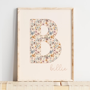 May include: A framed print with a cream background, displaying a floral "B". The letter is filled with a pattern of small flowers in pink, blue, and yellow. The name "billie" is written in cursive script below the letter.
