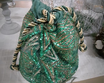 May include: Emerald green drawstring bag with gold and silver embellishments. The bag features a chain strap and a decorative rope trim. The bag is covered in sequins and glitter, creating a sparkling effect. The bag is a stylish accessory.