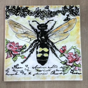 Pode incluir: Azulejo de cerâmica quadrado com uma ilustração detalhada de uma vespa. A vespa tem marcas amarelas e pretas e asas transparentes. O azulejo é decorado com rosas vermelhas e detalhes florais pretos, com escrita manuscrita na parte inferior.