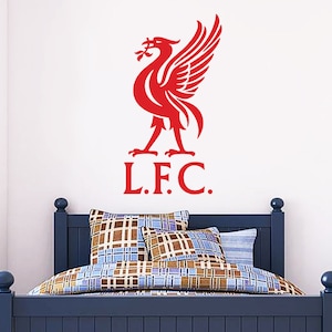 May include: Red Liverpool Football Club logo with a bird and the letters L.F.C. on a white wall above a blue bed with brown and blue patterned bedding.