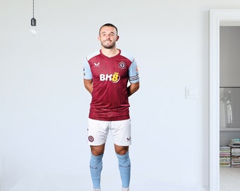 以下が含まれることがあります： マロンと白のジャージを着たサッカー選手。ジャージの前面には「Bhk8」の文字が書かれている。選手は白いショートパンツと青い靴下を履いている。選手は白い床の上に立っている。
