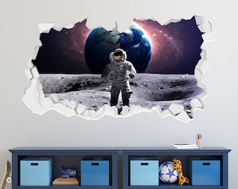 Könnte beinhalten: Ein blaues Bücherregal mit zwei Regalbrettern, auf denen verschiedene bunte Aufbewahrungsboxen und Spielzeug stehen. Das Bücherregal steht vor einer weißen Wand mit einem 3D-Wandaufkleber eines Astronauten, der auf dem Mond steht, mit der Erde im Hintergrund.