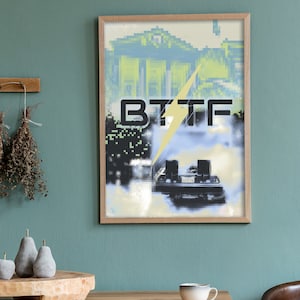 Puede incluir: Una impresión enmarcada de un coche futurista conduciendo por una ciudad pixelada con el texto "BTTF" en letras negras. El coche está parcialmente oscurecido por un rayo blanco.