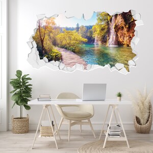 May include: A wall decal featuring a scenic landscape with a waterfall, a wooden walkway, and a lake. The decal is designed to look like a hole in the wall, creating a 3D effect.