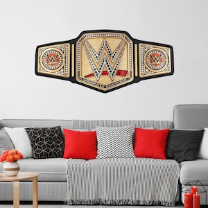 May include: A black and gold wrestling championship belt with a red stripe and the words "Undisputed Champion". The belt is on a white wall above a gray couch with black and white pillows.
