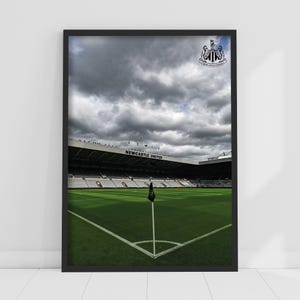May include: A black and white photo of a soccer stadium with a cloudy sky. The stadium is empty and the grass is green. The words "NEWCASTLE UNITED" are visible on the stadium.