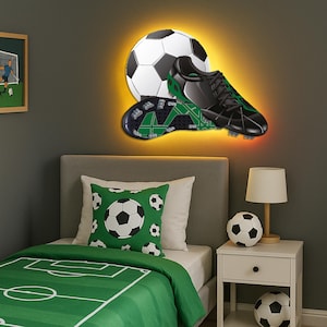 May include: A bedroom decorated with a soccer theme. The image shows a soccer ball, black cleats with green details, and a soccer ball-shaped lamp. The bed has a green duvet cover with a soccer field design and a pillow with soccer ball patterns.