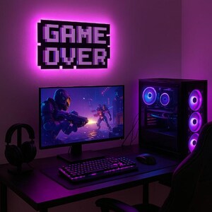 May include: A purple and black gaming setup with a computer monitor displaying a video game, a keyboard, a mouse, a gaming chair, and a neon sign that reads "GAME OVER".