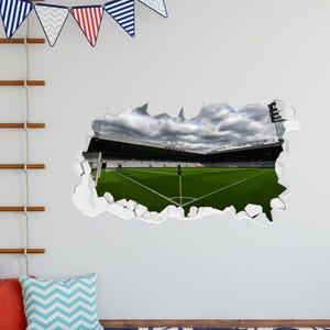 K&ouml;nnte beinhalten: Ein Wandaufkleber mit einem realistischen 3D-Effekt eines Fu&szlig;ballstadions mit einem gr&uuml;nen Rasen und einem bew&ouml;lkten Himmel. Der Aufkleber scheint aus der Wand gerissen zu sein und erzeugt so einen dramatischen Effekt.