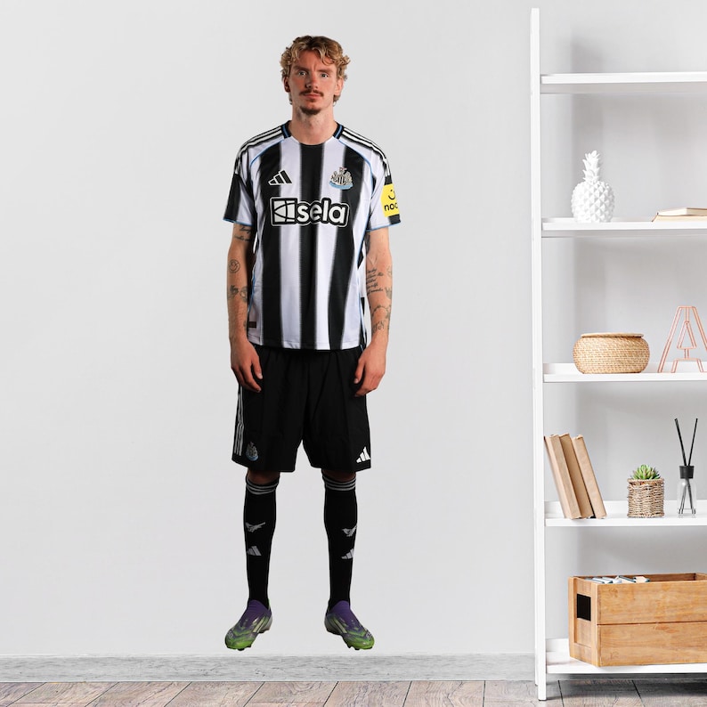 May include: A person in a black and white striped football shirt with the word "Kisela" on the front. They are wearing black shorts, black socks, and green and black football boots. The shirt has a yellow patch on the right sleeve.