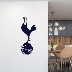 Puede incluir: Una calcomanía de logotipo del club de fútbol Tottenham Hotspur azul y blanco que presenta un gallo de pie sobre un balón de fútbol.