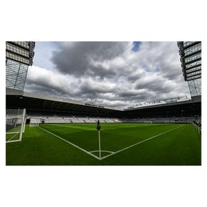 Puede incluir: Un campo de f&uacute;tbol vac&iacute;o con una bandera negra en el centro. El campo est&aacute; rodeado por un gran estadio con asientos negros y un letrero que dice "NEWCASTLE UNITED".