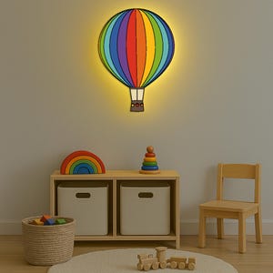 May include: A vibrant, rainbow-striped hot air balloon wall light. The light is mounted on a neutral wall above a wooden shelf with toys, including a rainbow arch, a stacking toy, and a wooden train. A small wooden chair is also visible.