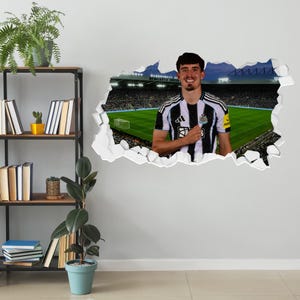 May include: A wall decal featuring a soccer player in a black and white striped jersey, with a stadium backdrop. The player is smiling and has his hand over his heart. The decal has a 3D effect, with a torn wall revealing the image.