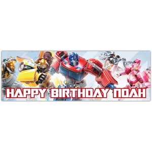 May include: A rectangular banner featuring various Transformers characters in action poses. The banner has the text "HAPPY BIRTHDAY NOAH" in red block letters. The background is a light blue colour.