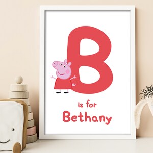 Puede incluir: Una impresión enmarcada en blanco con una gran letra B roja y un cerdo rosa de dibujos animados. El texto "is for Bethany" está debajo de la letra.