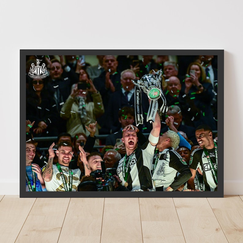 May include: A group of people celebrating with a trophy. The trophy is silver with black and green accents. The people are wearing black and white uniforms with green accents. The trophy has the text "Carabao Cup Final" on it.