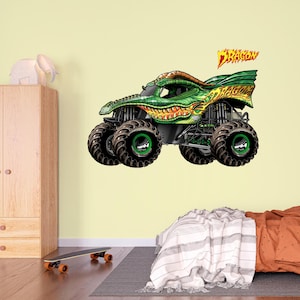 May include: A green and yellow monster truck with the word "DRAGON" in flame-like lettering. The truck has large black tires with green rims and a detailed dragon-scale design on the body. The image is a vibrant illustration.