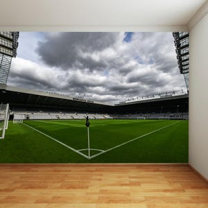 Puede incluir: Una vista panor&aacute;mica de un estadio de f&uacute;tbol con un campo verde, l&iacute;neas blancas y una bandera negra. El estadio est&aacute; casi vac&iacute;o con algunas personas en las gradas. El cielo est&aacute; nublado y gris.