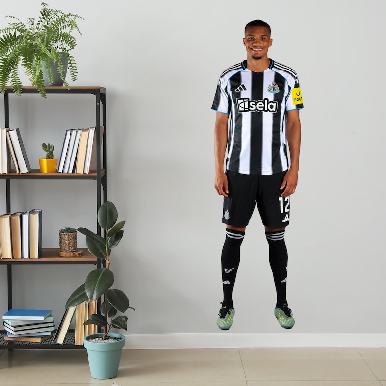 May include: A person wearing a black and white striped soccer jersey with the word "Isela" on the front. The person is also wearing black shorts with the number 12, black socks, and green cleats. The jersey has a yellow patch on the right sleeve.